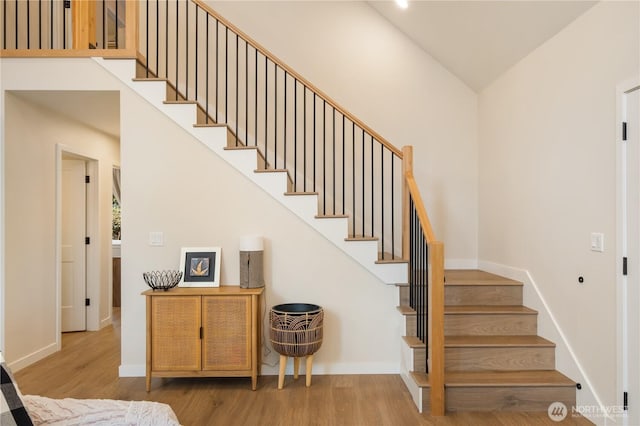 staircase featuring wood finished floors, a towering ceiling, and baseboards