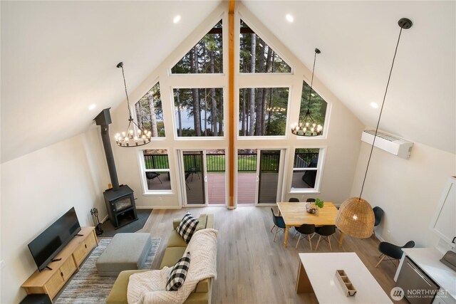living area with high vaulted ceiling, a chandelier, a wood stove, and wood finished floors