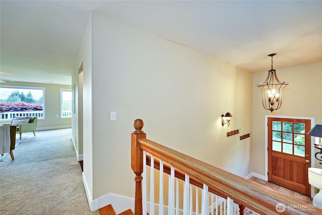 foyer entrance featuring a chandelier, baseboards, and carpet