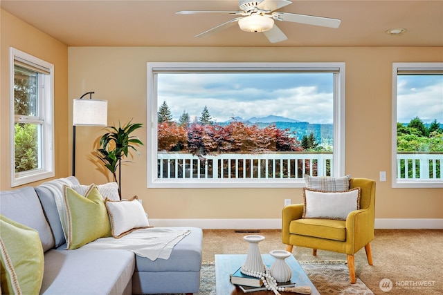 carpeted living room featuring ceiling fan, baseboards, plenty of natural light, and a mountain view