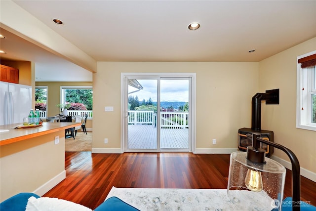 living room featuring a wood stove, wood finished floors, baseboards, and recessed lighting