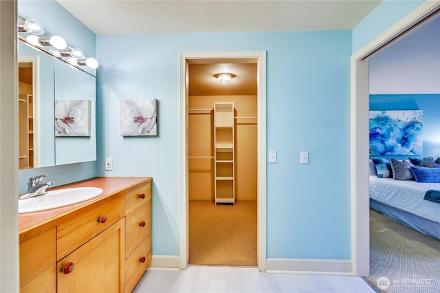 ensuite bathroom featuring vanity, a walk in closet, and baseboards