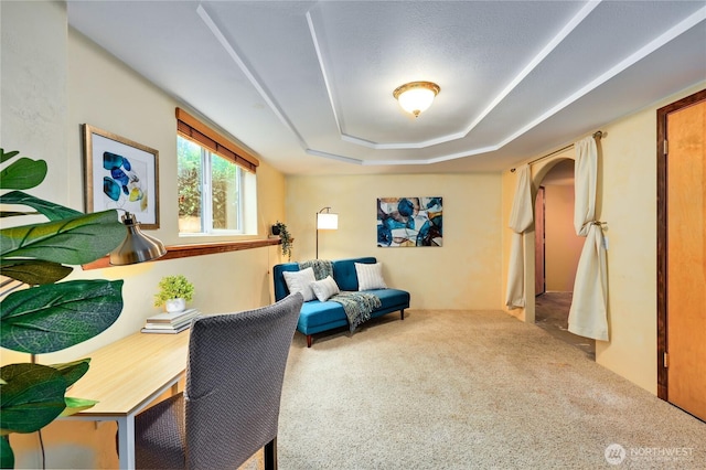 living area with carpet flooring, a raised ceiling, and arched walkways
