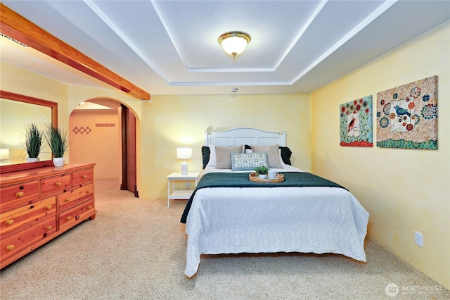 carpeted bedroom featuring arched walkways and a tray ceiling