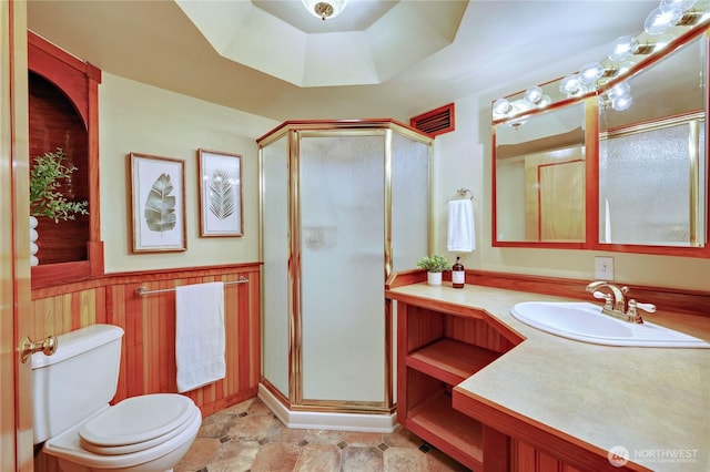 full bathroom with a stall shower, toilet, vanity, and wainscoting