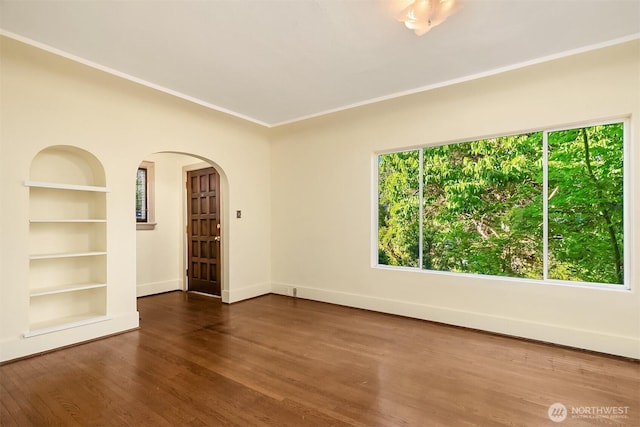 unfurnished room with built in features, arched walkways, baseboards, crown molding, and wood finished floors