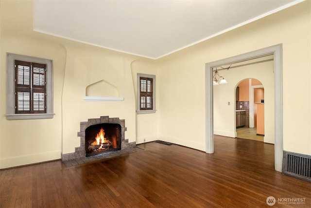 unfurnished living room with a fireplace with flush hearth, wood finished floors, plenty of natural light, arched walkways, and crown molding