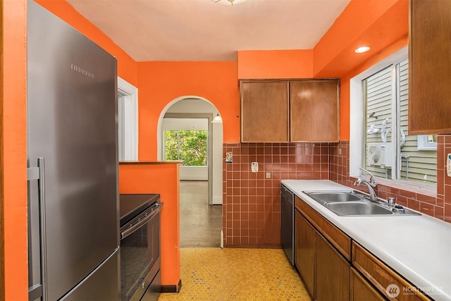 kitchen featuring stainless steel appliances, a sink, light countertops, tile walls, and brown cabinetry