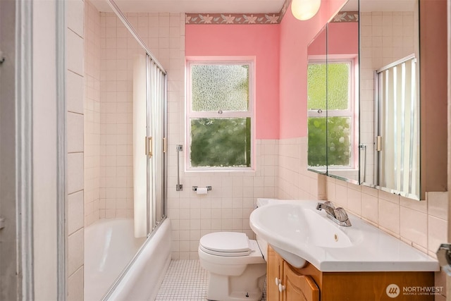 full bathroom with tile walls, toilet, vanity, tile patterned floors, and shower / bath combination with glass door