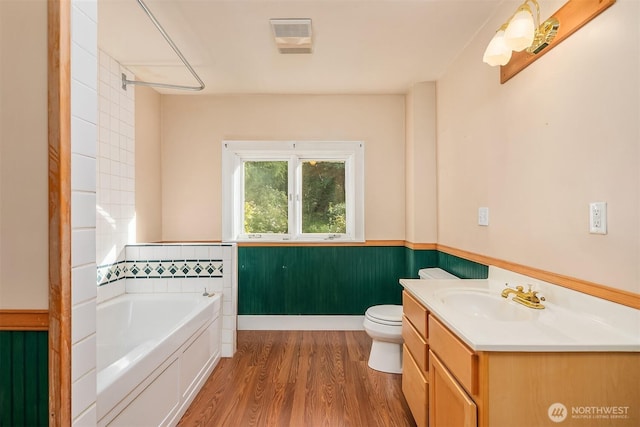 full bathroom with a wainscoted wall, a bath, wood finished floors, toilet, and vanity