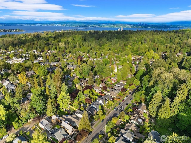 view of property location with a heavily wooded area, a nearby body of water, and nearby suburban area