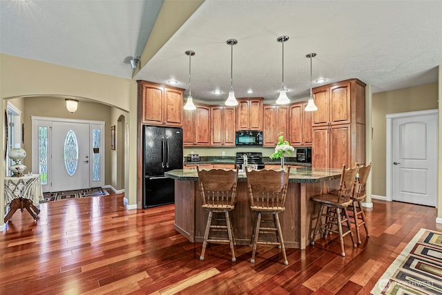 108 Reynolds Rd, Castle Rock, WA 98611 - kitchen with black appliances, arched walkways, brown cabinetry, dark wood-style flooring, and a kitchen bar