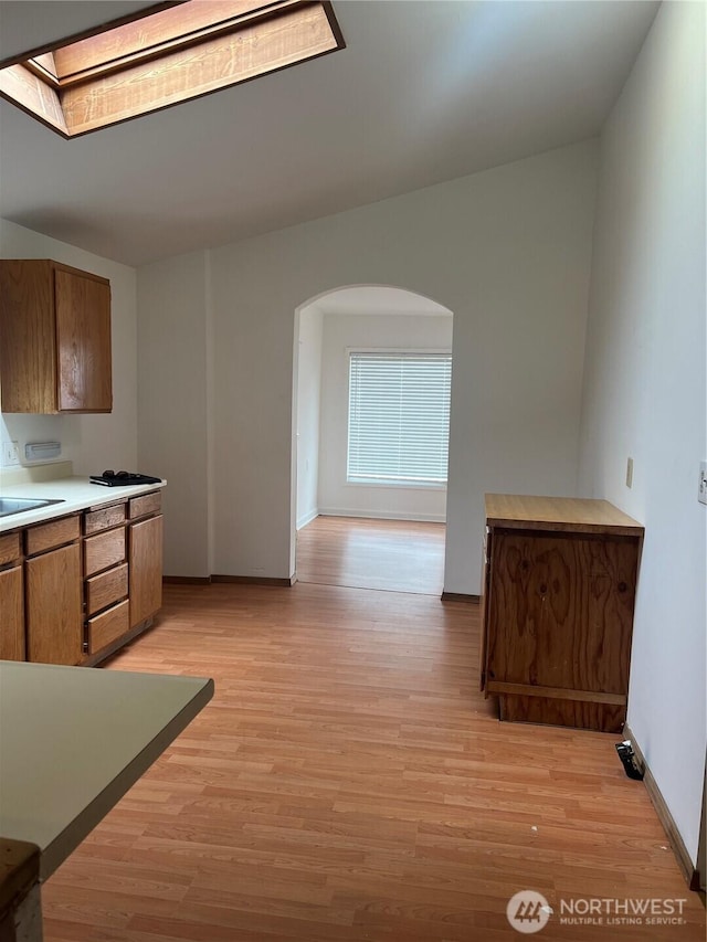 28 N Fir St, Omak, WA 98841 - kitchen featuring arched walkways, brown cabinets, light wood-style flooring, baseboards, and light countertops