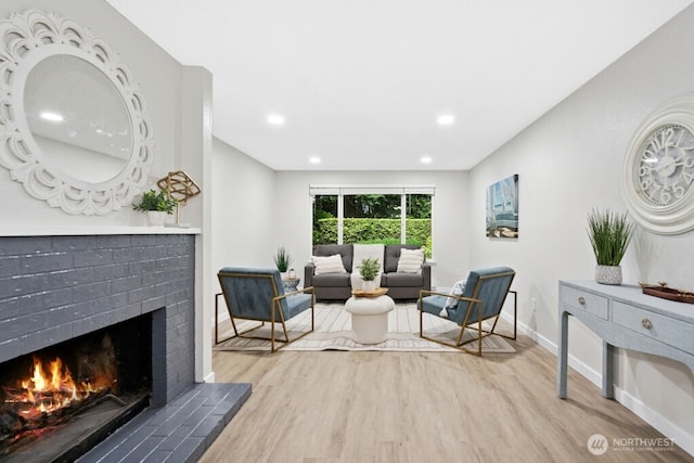 sitting room with wood finished floors, a brick fireplace, baseboards, and recessed lighting