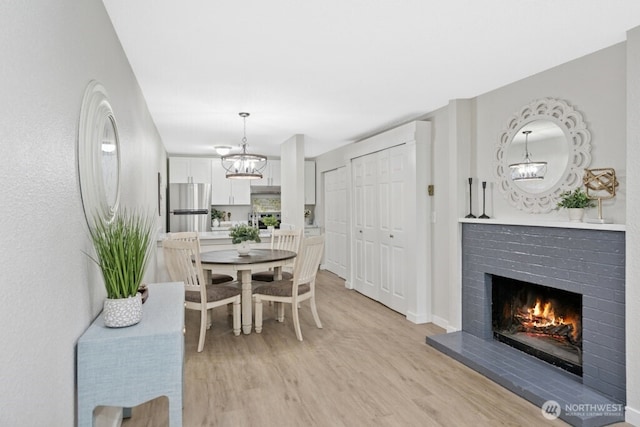 dining area with light wood finished floors, a chandelier, a brick fireplace, and baseboards