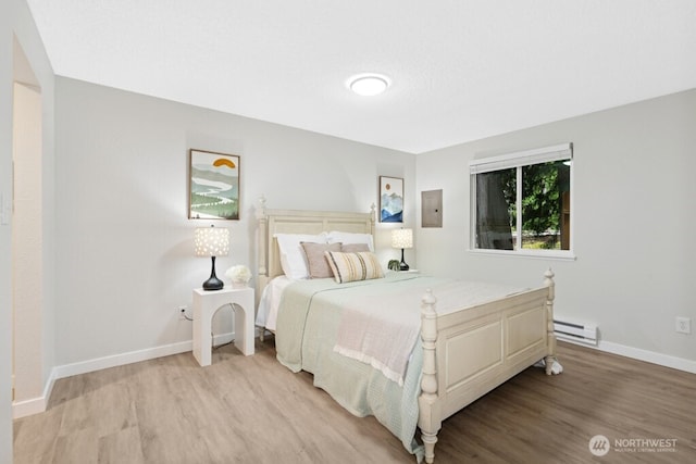 bedroom featuring light wood finished floors, a baseboard heating unit, and baseboards