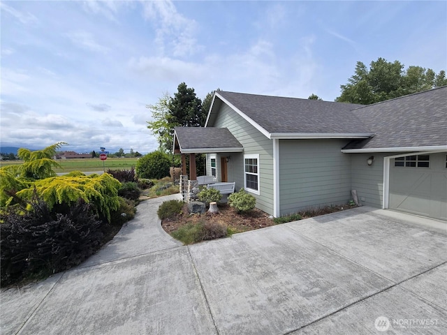 view of side of property with roof with shingles, an attached garage, concrete driveway, and covered porch