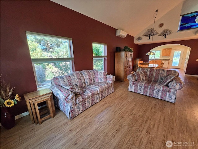 living area with high vaulted ceiling, wood finished floors, an AC wall unit, and arched walkways