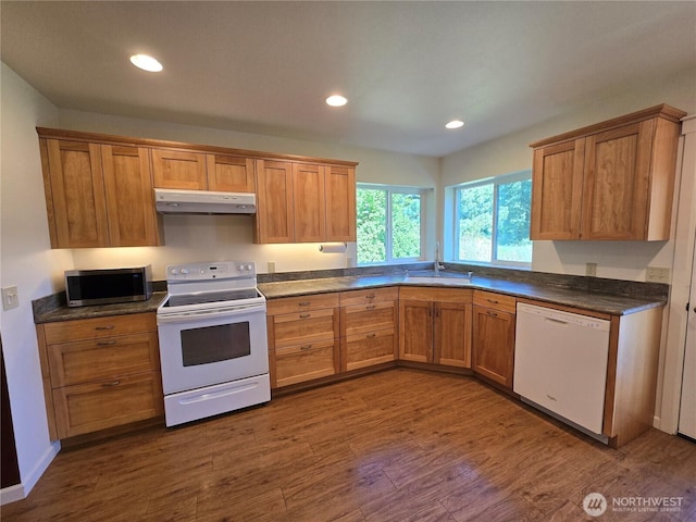 kitchen featuring white appliances, under cabinet range hood, dark countertops, dark wood-style flooring, and recessed lighting