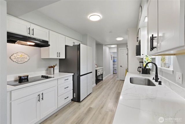 16015 Lange Rd, Mount Vernon, WA 98273 - kitchen with under cabinet range hood, black electric cooktop, a sink, white cabinets, and freestanding refrigerator