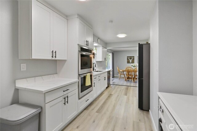 16015 Lange Rd, Mount Vernon, WA 98273 - kitchen featuring appliances with stainless steel finishes, light wood-style flooring, a sink, white cabinets, and baseboards