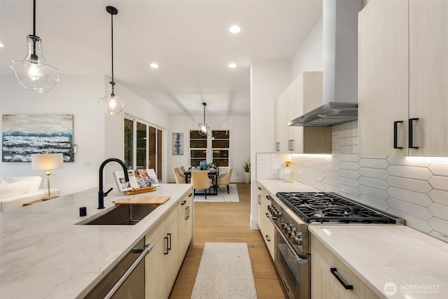 kitchen with wall chimney range hood, a sink, stainless steel stove, light wood-type flooring, and light stone countertops
