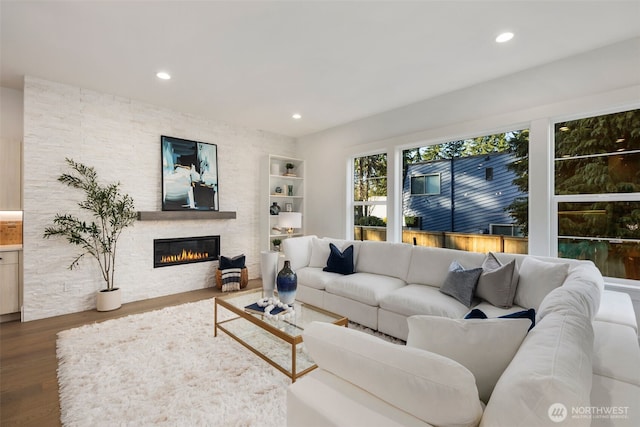 living area featuring wood finished floors, recessed lighting, a stone fireplace, and built in features