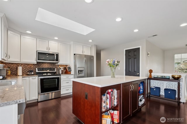 4019 N Vassault St, Tacoma, WA 98407 - kitchen with appliances with stainless steel finishes, a skylight, dark wood finished floors, decorative backsplash, and white cabinets