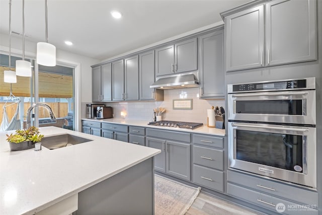 18230 134th Ave E, Puyallup, WA 98374 - kitchen featuring gray cabinets, appliances with stainless steel finishes, under cabinet range hood, a sink, and tasteful backsplash