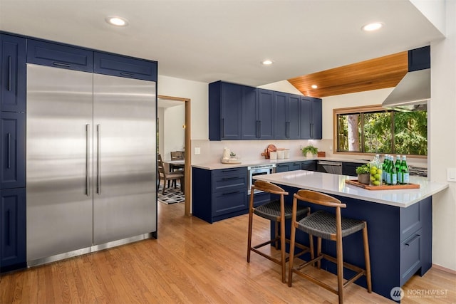 6160 W Mercer Way, Mercer Island, WA 98040 - kitchen featuring appliances with stainless steel finishes, blue cabinets, a kitchen breakfast bar, light countertops, and light wood-type flooring
