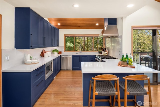 6160 W Mercer Way, Mercer Island, WA 98040 - kitchen featuring blue cabinets, stainless steel appliances, wall chimney exhaust hood, a peninsula, and recessed lighting