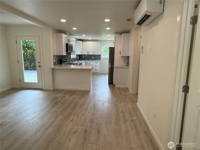 kitchen with a wall mounted AC, stainless steel appliances, light wood-style flooring, white cabinetry, and recessed lighting