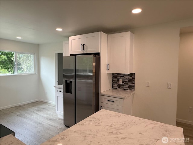 kitchen featuring stainless steel fridge, light stone countertops, white cabinetry, light wood-style flooring, and backsplash