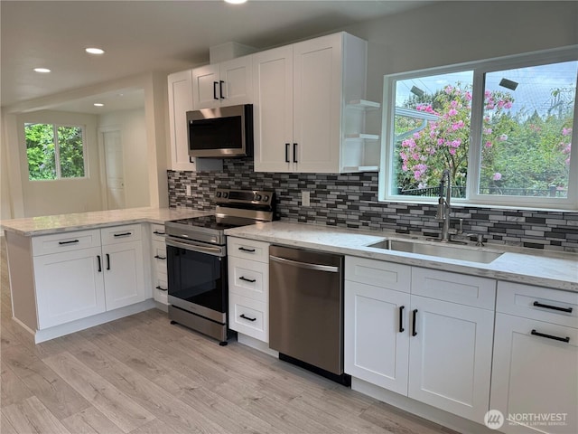 kitchen with stainless steel appliances, a sink, a peninsula, white cabinets, and recessed lighting
