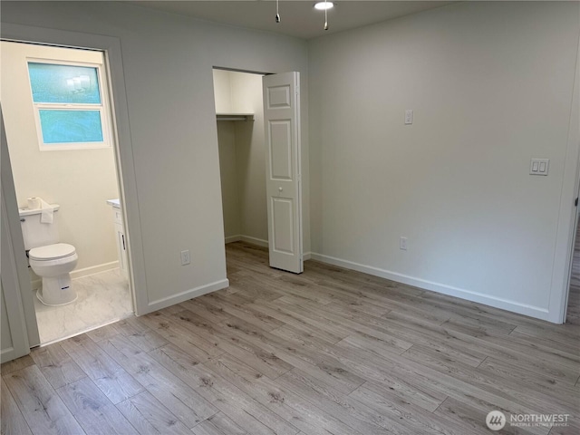 unfurnished bedroom with wood finished floors, baseboards, ensuite bath, and a closet