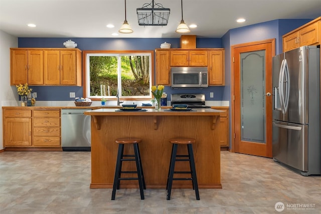3120 Wave Dr, Everett, WA 98203 - kitchen with stainless steel appliances, a kitchen island, a breakfast bar area, brown cabinetry, and recessed lighting
