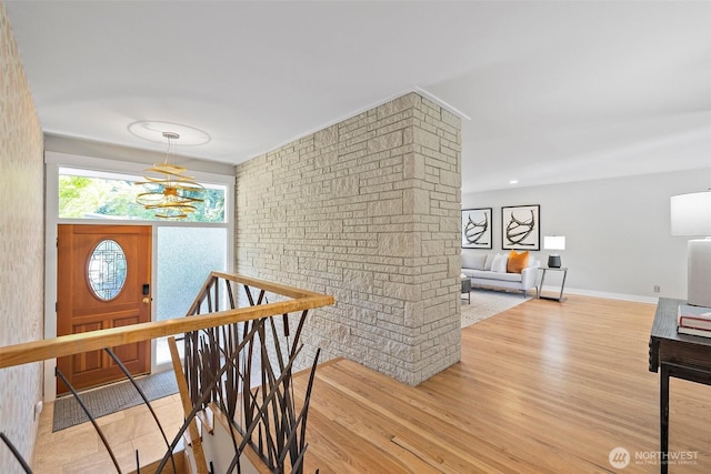 hall with an upstairs landing, light wood-type flooring, a chandelier, and baseboards