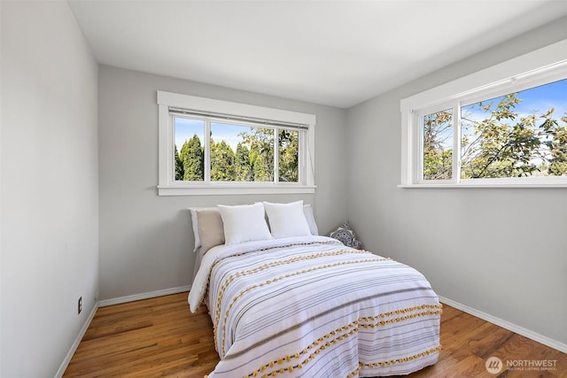 bedroom with multiple windows, wood finished floors, and baseboards