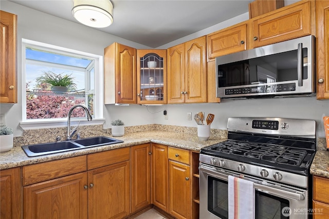 kitchen with stainless steel appliances, a sink, glass insert cabinets, and brown cabinetry