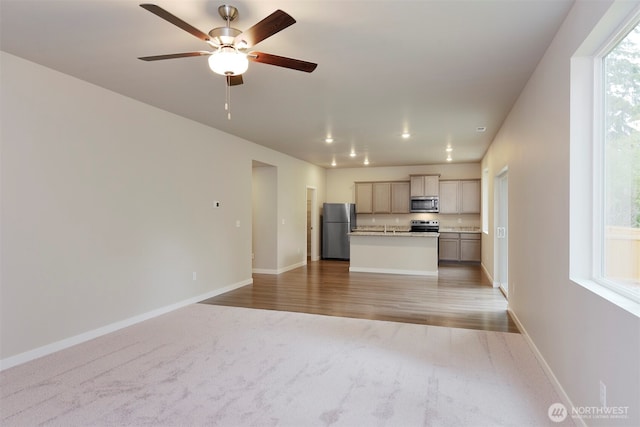 8507 13th Ave E, Tacoma, WA 98445 - unfurnished living room featuring light carpet, baseboards, ceiling fan, and light wood-style flooring
