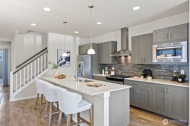 938 SW 97th St, Seattle, WA 98106 - kitchen featuring wall chimney exhaust hood, appliances with stainless steel finishes, gray cabinetry, backsplash, and light wood finished floors