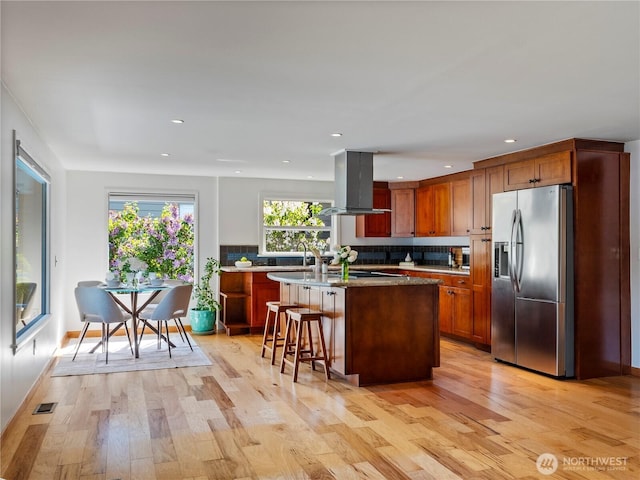 6341 NE Balzow Rd, Suquamish, WA 98392 - kitchen featuring stainless steel refrigerator with ice dispenser, island range hood, light wood finished floors, tasteful backsplash, and an island with sink