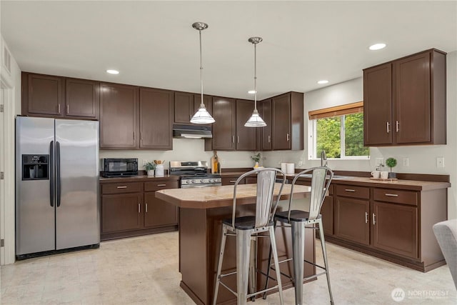 kitchen with appliances with stainless steel finishes, dark brown cabinetry, under cabinet range hood, a breakfast bar area, and recessed lighting