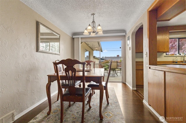 dining space featuring dark wood-style floors, a chandelier, arched walkways, a textured ceiling, and baseboards