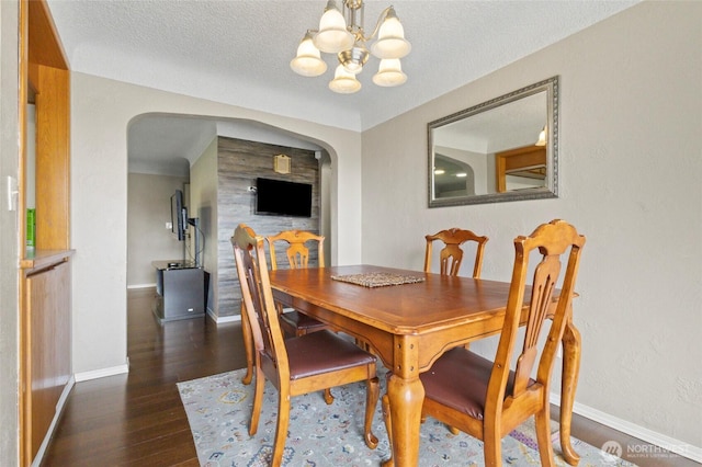 dining area featuring arched walkways, a chandelier, wood finished floors, baseboards, and a textured ceiling