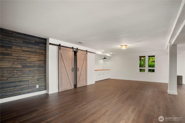 1420 Mitchell Rd, Lake Stevens, WA 98258 - unfurnished living room featuring a barn door, dark wood finished floors, wooden walls, baseboards, and an accent wall