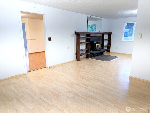 8927 178th Ave SW, Rochester, WA 98579 - unfurnished living room with a wood stove, wood finished floors, baseboards, and a textured ceiling
