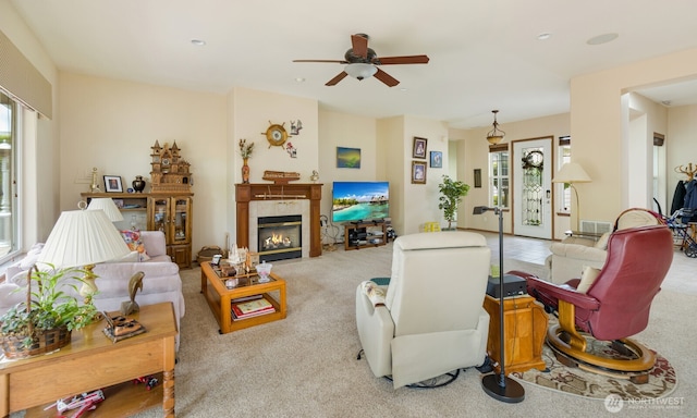 living area with ceiling fan, a glass covered fireplace, and carpet floors