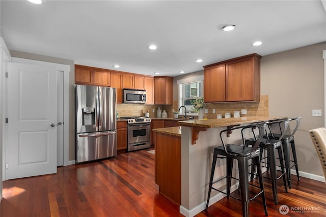 830 15th Ave Unit A, Seattle, WA 98122 - kitchen with stainless steel appliances, brown cabinetry, a peninsula, dark wood-type flooring, and recessed lighting