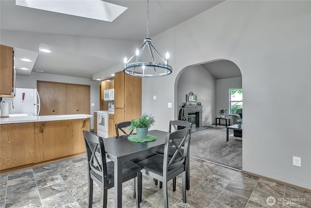 56065608 76th Street Ct E, Puyallup, WA 98371 - dining space with a chandelier, a skylight, arched walkways, a glass covered fireplace, and baseboards